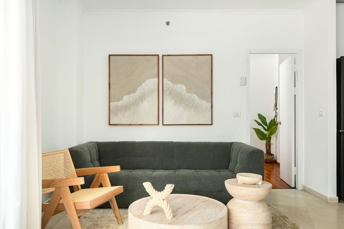 A living room with a dark green sofa, a wooden chair, and two round side tables with decorative items.