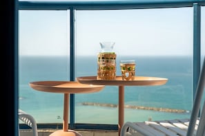 A table with two glasses of a beverage, a glass pitcher, and a view of the ocean through a window.