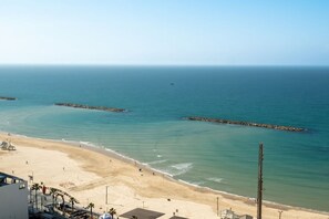 A beach with clear blue water, a sandy shore, and a few buildings in the foreground.