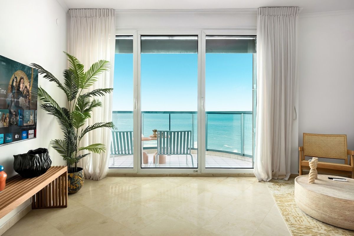 A room with a large sliding glass door leading to a balcony with a view of the ocean.