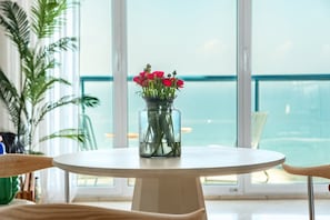 A round table with a vase of flowers and a view of the sea through large windows.