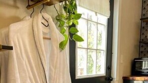 A white bathrobe hanging on a wooden hanger near a black door with a window.