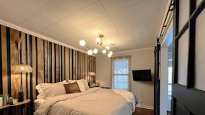 A bedroom with a large bed, wooden panel wall, and a TV on the wall.