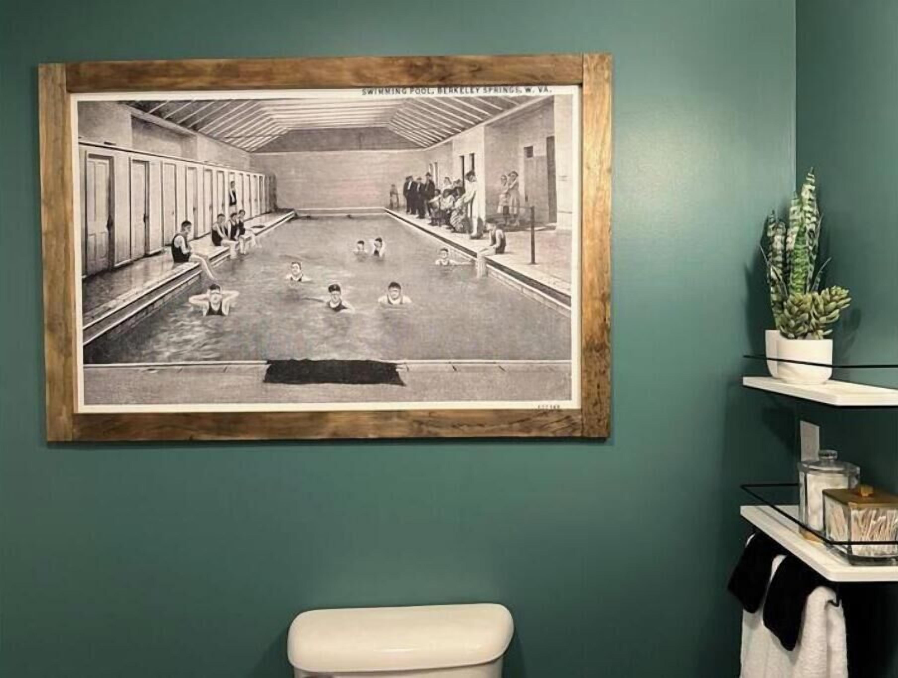 A framed black and white photograph of a swimming pool area with multiple lanes, a changing room, and a few people.
