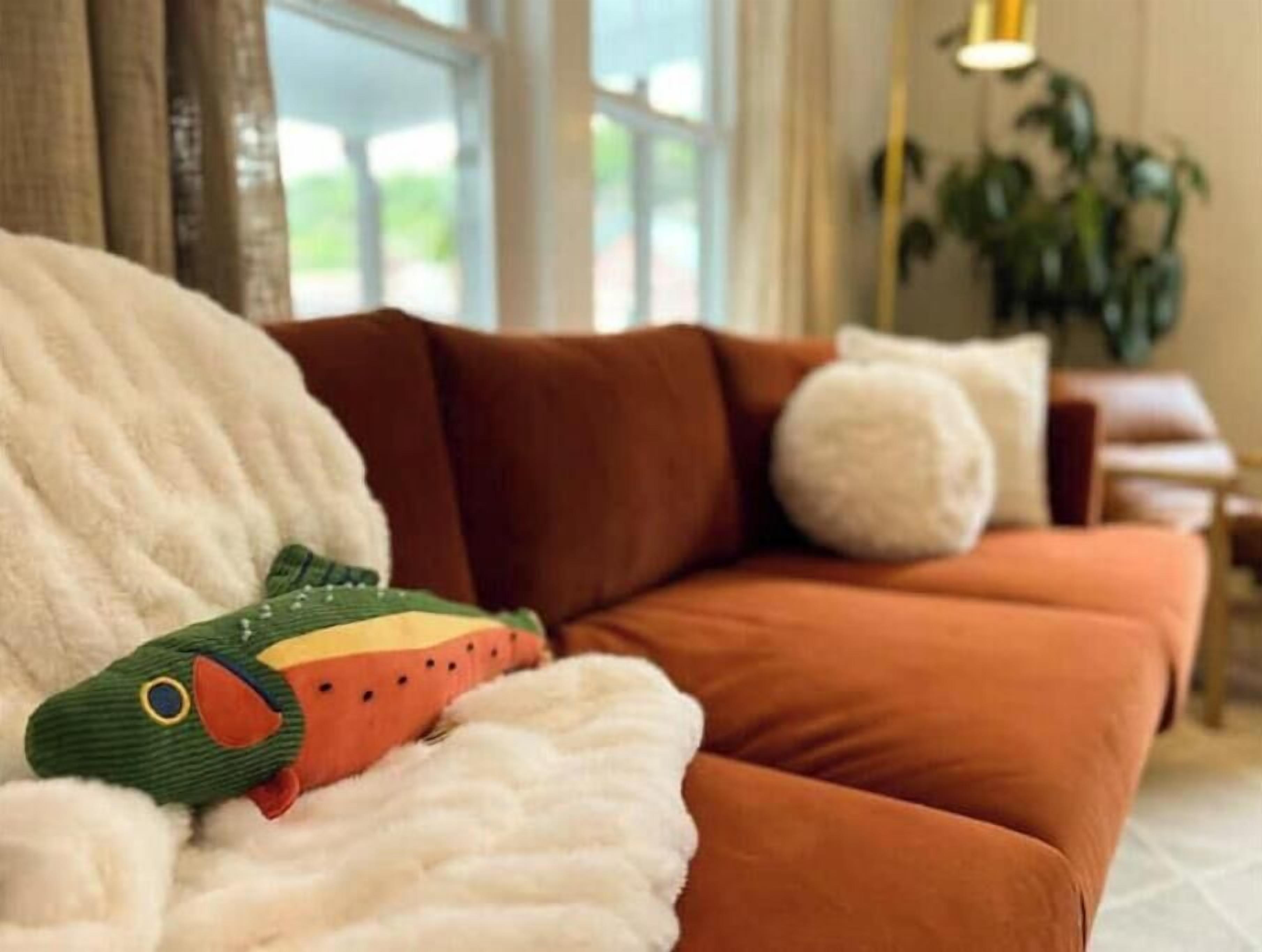 Un salon chaleureux avec un canapé marron, une couverture blanche et moelleuse, et un jouet en peluche vert.