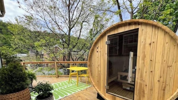 A wooden cabin with a glass door, a yellow table, and a green patterned rug on a wooden deck.