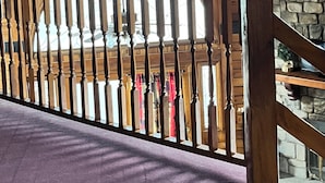 Interior de fusta amb un sostre alt, una paret de pedra i vista d'una habitació amb roba penjant.