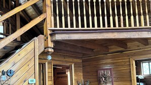 Interior d'una cabana de fusta amb un dormitori a la biga, una zona de dinar i un saló amb dos sofàs i una taula.
