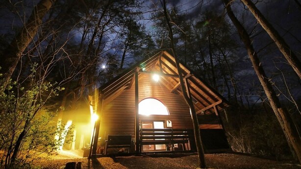 Una cabana de fusta amb una entrada gran i arqueada, envoltada d'arbres i il·luminada per llums exteriors.