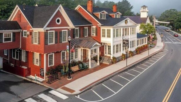 A row of red brick houses with white trim, a street with marked lanes, and a pedestrian crossing. - 3 Bedroom Townhouse (Stowe)