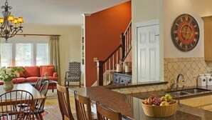A modern kitchen with a central island, a dining area with a sofa and chairs, and a staircase leading to another level. - 3 Bedroom Townhouse (Stowe)