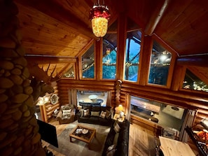 A log cabin interior with a fireplace, wooden furniture, and large windows. - Waters Edge Luxury Smoky Cabin • Swim Spa • Sauna • Mini Golf (Severeville)