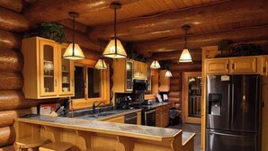 Interior de una cabaña rústica con cocina, que incluye armarios de madera, un refrigerador de acero inoxidable y una barra con taburetes.