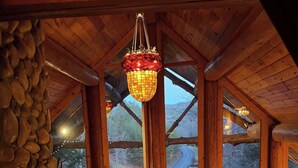 Interior de madera con un farol colgante, pared de piedra y ventanas con vistas a un paisaje nevado.