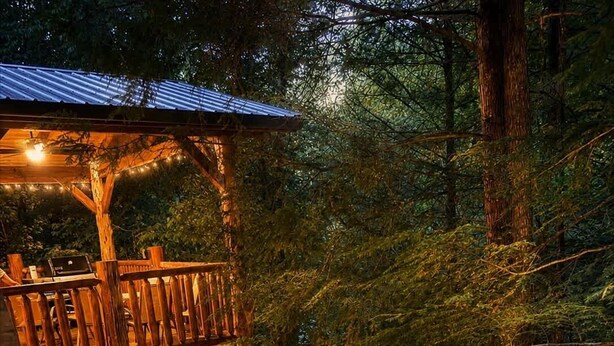 Una terraza de madera con jacuzzis, rodeada de árboles y luces colgantes.