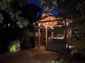 A wooden structure with a covered patio area, surrounded by trees and a stone pathway.