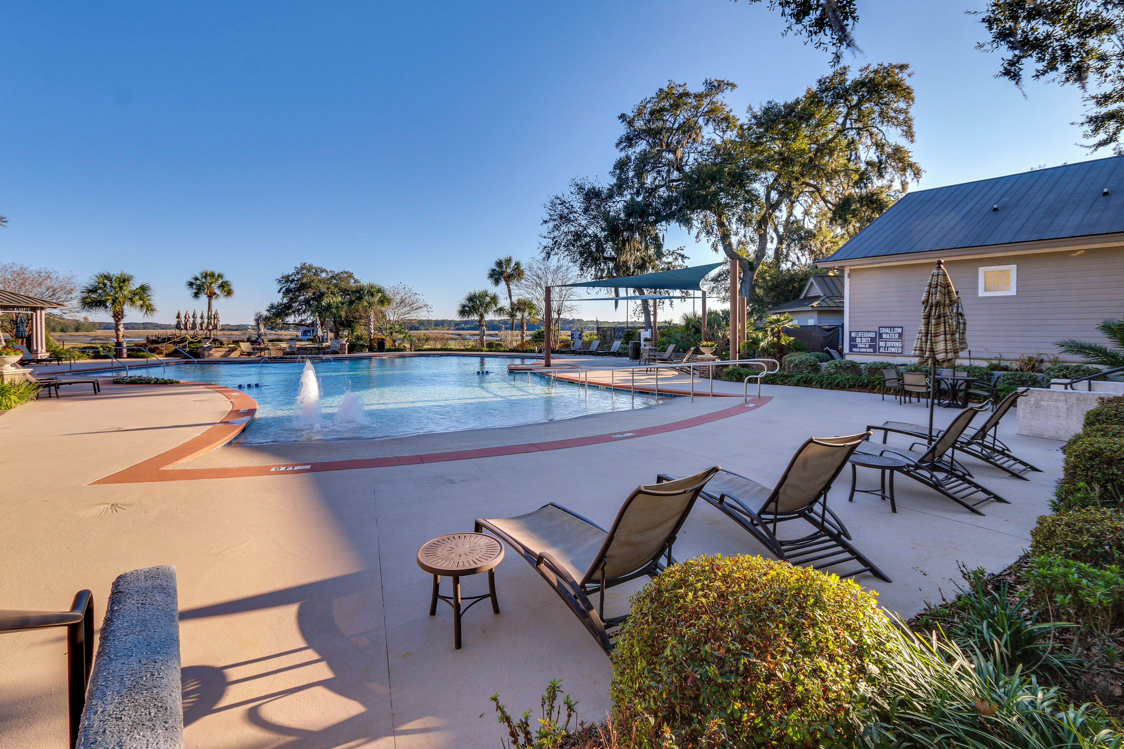 A pool area with lounge chairs, a small table, and a covered seating area.