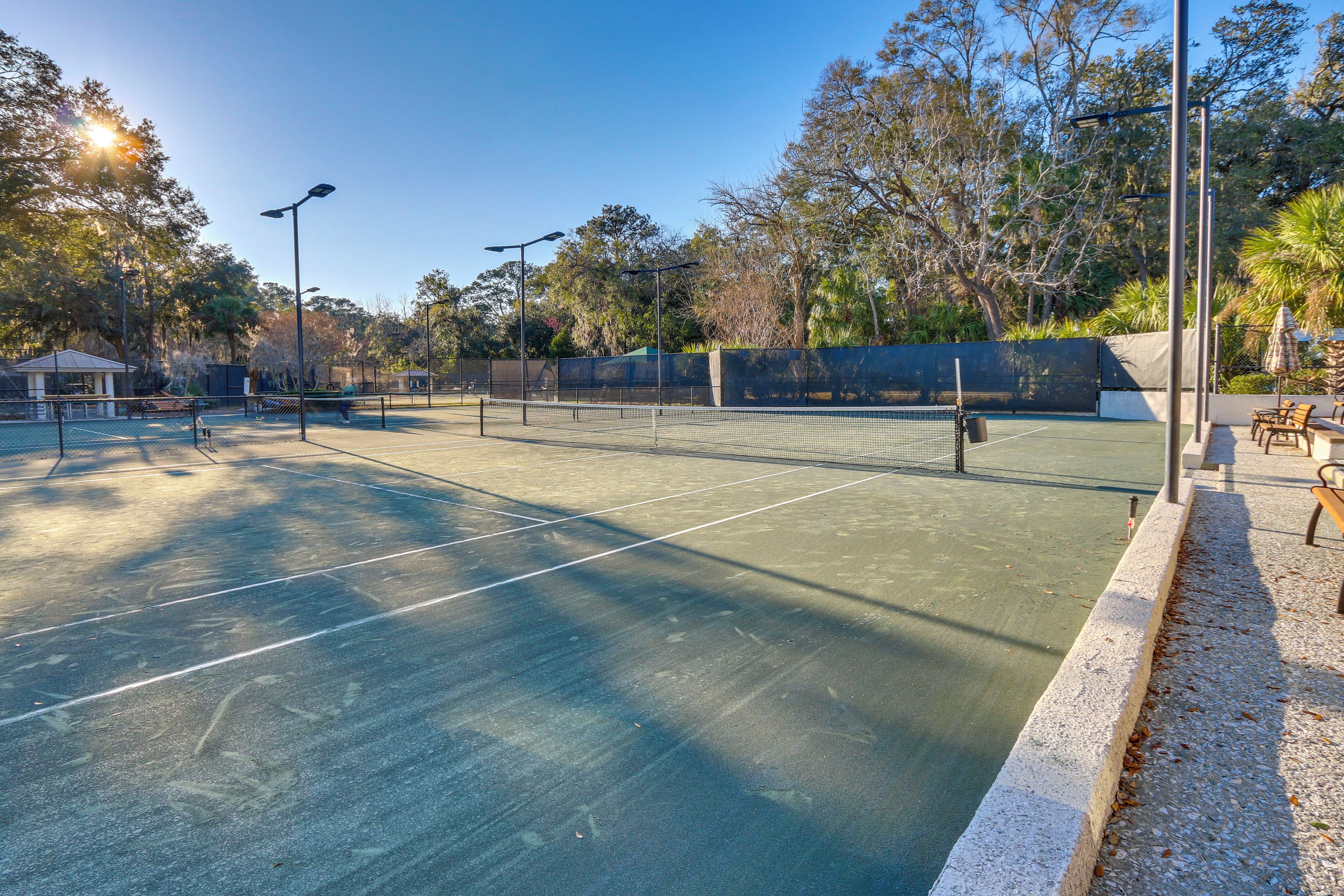An outdoor tennis court with a net, surrounded by trees and benches.