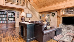 A spacious living room with a fireplace, leather sofa, bookshelves, and a staircase. - Big Sky Lodge 5 Br + Bonus-4 Ensuites, Mt Views, hot tub, game room,Pet friendly (McDowell County)