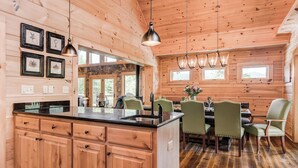 A wooden cabin interior with a kitchen island, dining area, and wooden walls. - Big Sky Lodge 5 Br + Bonus-4 Ensuites, Mt Views, hot tub, game room,Pet friendly (McDowell County)