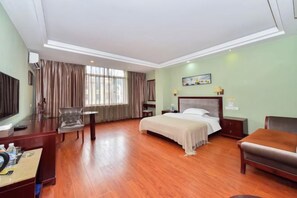 Una habitación de hotel con cama, escritorio, silla, televisor y ventana con cortinas.