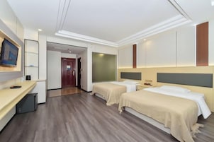 Habitación de hotel con dos camas, un escritorio, un televisor y una puerta que da a otra habitación.