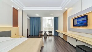 Habitación de hotel con cama, escritorio, televisor y balcón con cortinas.