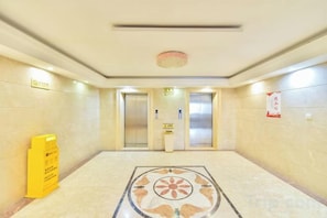 A hotel lobby with a tiled floor, two elevators, a yellow information stand, and a patterned floor design. - Dong He Hotel (Dongxing)
