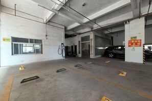 A parking garage with concrete floors, yellow safety cones, and a black car parked in the distance. - Dong He Hotel (Dongxing)