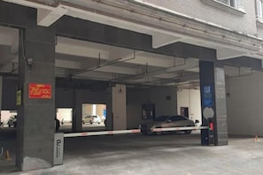 Un aparcamiento con pilares de hormigón, entrada con barrera y señal de estacionamiento azul.