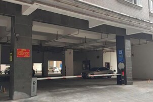 Un aparcamiento con pilares de hormigón, entrada con barrera y señal de estacionamiento azul.