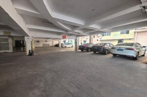 Un estacionamiento de varios niveles con varios automóviles estacionados, pisos de concreto y un edificio con señalización al fondo.