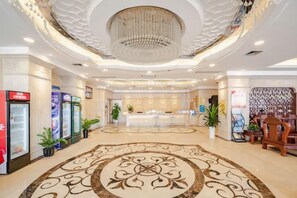 Un vestíbulo de hotel con una recepción central, techo decorativo y alfombra estampada.