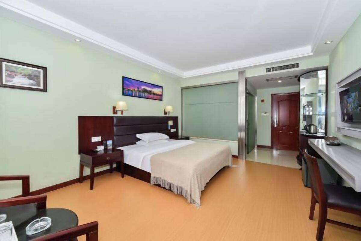 Quarto de hotel com cama, mesas de cabeceira, escrivaninha e televisão.
