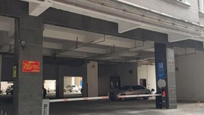 Entrada a un estacionamiento con un sistema de acceso vehicular, señal de estacionamiento y un pilar con un letrero rojo.