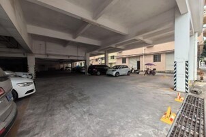 Un estacionamiento subterráneo con varios coches aparcados, pilares de hormigón y una pasarela para peatones.