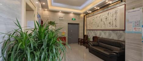 A lobby with a reception desk, a sofa, a large potted plant, and a framed artwork on the wall.