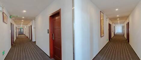 A long, narrow hotel corridor with a patterned carpet, doors on both sides, and a red door in the center.