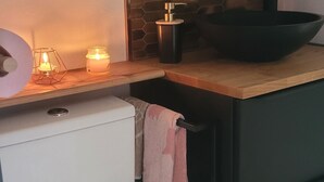 Una cocina compacta con inodoro blanco, encimera de madera, salpicadero con motivo hexagonal y un lavamanos negro.