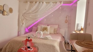 Un dormitorio con una cama, una mesa con una botella y vasos, una silla y una mesa de comedor.