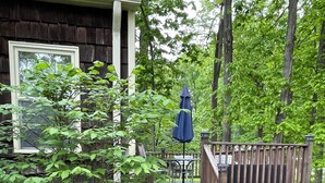 A wooden deck with a blue umbrella, a small garden with various plants, and a staircase leading to a porch.