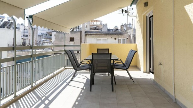 A balcony with a table and chairs, a metal railing, and a view of buildings in the background. - Kosmos Serenity - 1BR, Central Athens (Athina)