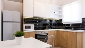 A modern kitchen with white cabinets, a black tiled backsplash, a microwave, a coffee maker, and a potted plant.