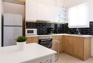 Et moderne køkken med hvide skabe, en backsplash med sorte fliser, en mikrobølgeovn, kaffemaskine og en potteplante.
