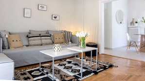 A modern living room with a grey sofa, two white side tables, a patterned rug, and a vase of white flowers.