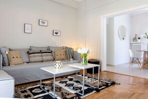 En moderne stue med en grå sofa, to hvide sofaborde, en gulvtæppe med mønster og en vase med hvide blomster.