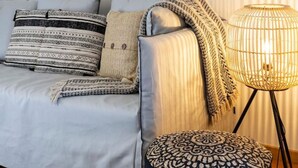 A modern living room with a grey sofa, patterned cushions, a black ottoman, and a floor lamp.