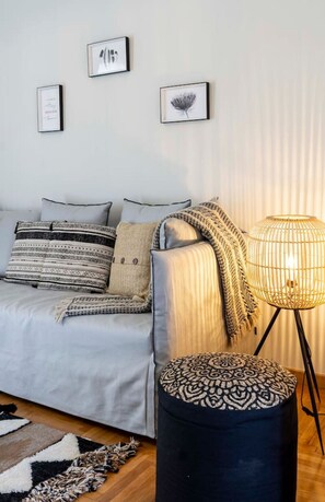 En moderne stue med en grå sofa, mønstrede puder, en sort fodsæde og en gulvlampe.