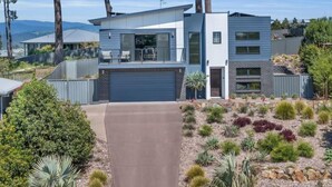 Et moderne hus i to etager med fladt tag, garage og en anlagt have med forskellige planter.