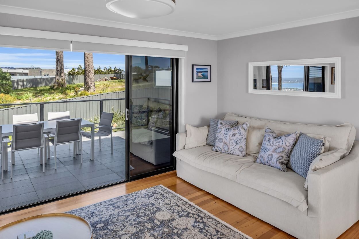 A modern living room with a sofa, a dining table with chairs, and a large sliding glass door leading to an outdoor patio.